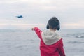 A boy in a red jacket and headphones smiling and shows his finger on the plane. Landing plane above sea waves in stormy weather Royalty Free Stock Photo