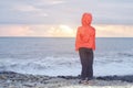 Boy in red jacket with hood standing back at the seashore. Sea w Royalty Free Stock Photo