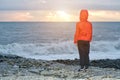 Boy in red jacket with hood standing on the beach. Sunset and waves Royalty Free Stock Photo