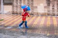 Boy with red raincoat disguised with umbrella splashes in a puddle of water Royalty Free Stock Photo