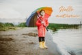 Boy in a red raincoat and yellow rubber boots stands at river bank and holding rainbow umbrella. School kid standing Royalty Free Stock Photo