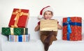 Boy in red santa helper hat with gift boxes sit on sofa. White background. Christmas holiday concept Royalty Free Stock Photo