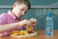 A boy in a red shirt dips chicken nuggets into ketchup before eating it and drinks  water from a bottle Royalty Free Stock Photo