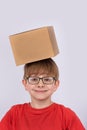 Boy in red shirt and glasses smiling and holding cardboard box on his head. Vertical frame