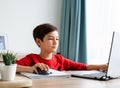 A boy in red shirt a hand on computer`s mouse focusing on study writing on paper, homeschool concept. Royalty Free Stock Photo