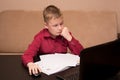 A boy in red shirt sits at a black table and does homework, a child in quarantine on distance learning