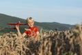 Boy in red T-shirt plays with toy plane in wheat field. Concept of flights and travel with children.Mountains background Royalty Free Stock Photo