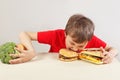 Boy in red at the table chooses between fastfood and vegetable and fruits on white background