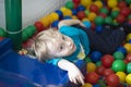 The boy rides from the children's slide and lies in the pool with colorful balls indoors. Royalty Free Stock Photo