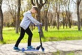 The boy is riding a scooter on the sidewalk path in the park