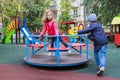 boy rolls girl in pink jacket on carousel in yard at playground outdoors Royalty Free Stock Photo