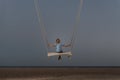 Boy on rope swing in the evening on beach. Child is swinging at twilight. Magic surreal zen landscape Royalty Free Stock Photo
