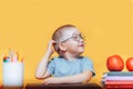 Boy in round glasses in a shirt and sitting at desk and thinking, doing homework, on a yellow background. back to school Royalty Free Stock Photo