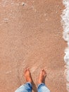 boy's feet standing on brown sandy beach with sea wave