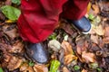 Boy`s legs in red jumpsuit on fallen autumn foliage after the rain. A child in rubber boots and mud is walking after the rain on