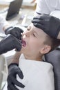 Boy`s open mouth during the tooth extraction procedure. The assistant holds the patient`s head and the doctor holds ticks in h