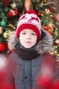 Boy`s portrait outdoors. Blured cristmas tree at background. Royalty Free Stock Photo