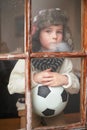 Boy, sad and ball by window for soccer in house during winter with rain for sports or fun game. Child, anxiety and Royalty Free Stock Photo