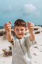 Boy with sand falling from his clnched fist, standing on beach. Family summer vacation by sea. Royalty Free Stock Photo