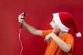 A boy in a Santa hat holds a phone in front of him and shouts cheerfully Royalty Free Stock Photo