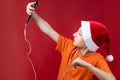 A boy in a Santa hat holds a phone in front of him and shouts cheerfully Royalty Free Stock Photo