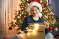 A boy in a santa hat opens a gift box next to a garlanded Christmas tree. Gifts for children. Dreams Come True Royalty Free Stock Photo