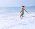 Boy in Santa hat runs to swim in ocean waves. Christams holiday Royalty Free Stock Photo