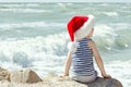 Boy in santa hat sitting on a rock. Sea shore. Back view Royalty Free Stock Photo