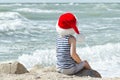 Boy in Santa hat sitting on a rock. Sea shore. Back view Royalty Free Stock Photo