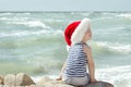 Boy in Santa hat and striped t-shirt sitting on the beach. Back view Royalty Free Stock Photo