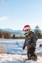 Boy with Santa red hat against a winter landscape background. Happy smiling child in the snow at Christmas standing beside tall