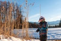 Boy with Santa red hat against a winter landscape background. Happy smiling child in the snow at Christmas standing beside tall