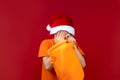 A boy in a Santa`s Christmas hat on a red background holds a gift bag in his hand and is very upset Royalty Free Stock Photo