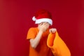 A boy in a Santa`s Christmas hat on a red background holds a gift bag in his hand and is very upset Royalty Free Stock Photo