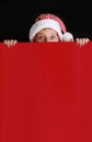 Boy in Santa`s hat surprised and holding red blank billboard for greetings. Royalty Free Stock Photo