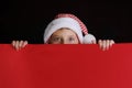 Boy in Santa`s hat surprised and holding red blank billboard for greetings. Royalty Free Stock Photo