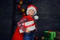 A boy in Santa`s hat holds gift box and red bag. Royalty Free Stock Photo