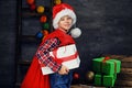 A boy in Santa`s hat holds gift box and red bag. Royalty Free Stock Photo