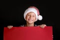 Boy in Santa`s hat surprised and holding red blank billboard for greetings. Royalty Free Stock Photo