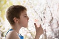 Boy of school age in breathing mask inhaler on a background of flowering trees. Home treatment. Prevention