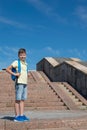Boy with a school bag stands tall against a blue sky, to the right of the stairs. Royalty Free Stock Photo