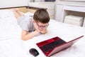 A boy, school boy lying in bed with a laptop and watching online translation, lesson, e-learning and education concept