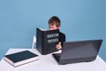 A boy in a school suit with a textbook on quantum physics during distance learning, copy space on a blue studio background