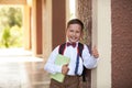 Boy schoolboy holding a textbook leaning against the wall of the school shows a hand sign of approval lifting his finger to the Royalty Free Stock Photo