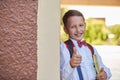 Boy schoolboy holding a textbook leaning against the wall of the school shows a hand sign of approval lifting his finger to the Royalty Free Stock Photo