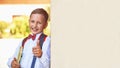 Boy schoolboy holding a textbook leaning against the wall of the school shows a hand sign of approval lifting his finger to the Royalty Free Stock Photo