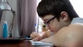 A boy, schoolboy sitting by the table, desk with laptop and doing homework at home, e-learning, distant lesson and online Royalty Free Stock Photo