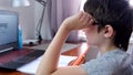 A boy, schoolboy sitting by the table, desk with laptop and doing homework at home, e-learning, distant lesson and online Royalty Free Stock Photo