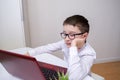 A boy, schoolboy in white formal shirt sitting by the table, desk with laptop and doing homework at home, e-learning, distant Royalty Free Stock Photo