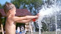 A boy of seven years, in swimsuit, bathe in the fountain, run around, squirt, have fun, on a hot summer day. Slow motion